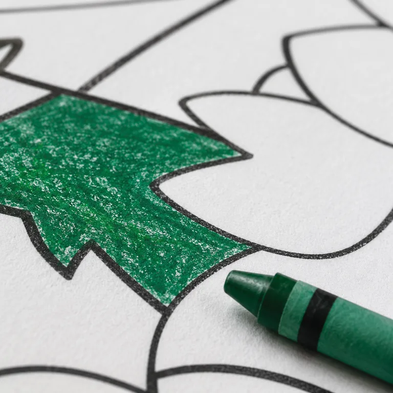 A close-up of a coloring page part-way done: one shape filled in with green crayon, the shapes around it still blank, the crayon resting alongside